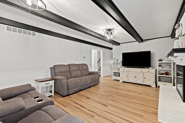 living area with beamed ceiling, light wood-style flooring, stairway, and a textured ceiling