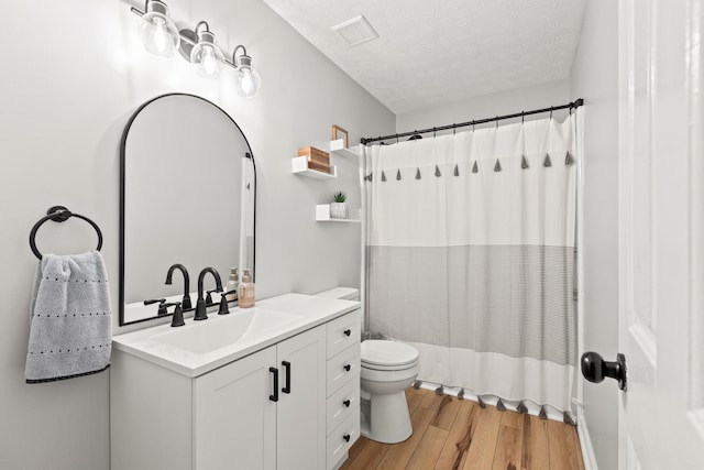 bathroom featuring a textured ceiling, wood finished floors, toilet, vanity, and shower / bathtub combination with curtain