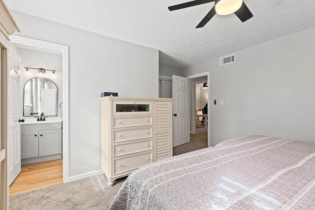 carpeted bedroom with ensuite bathroom, ceiling fan, and a sink