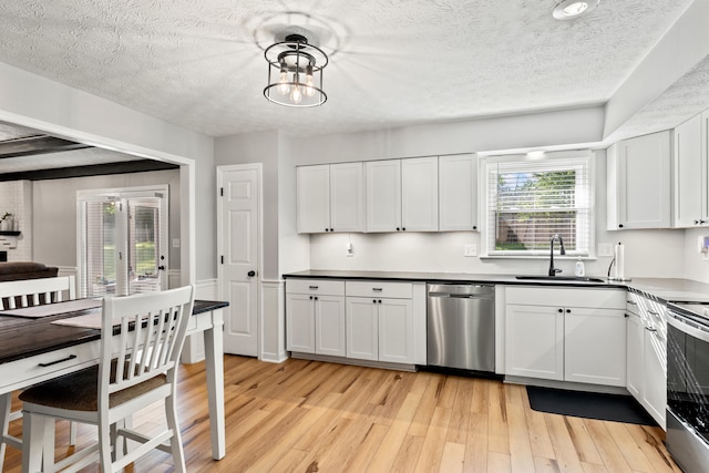 kitchen featuring appliances with stainless steel finishes, a sink, light wood finished floors, a textured ceiling, and white cabinets