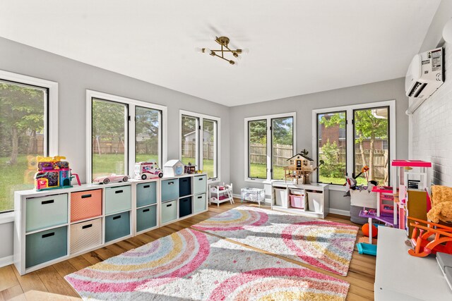 playroom with a wall mounted AC, light wood-style floors, and plenty of natural light