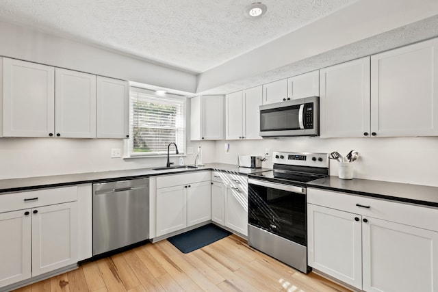 kitchen with stainless steel appliances, a sink, a textured ceiling, light wood-style flooring, and white cabinets