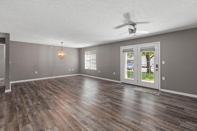 unfurnished living room featuring dark wood-type flooring, ceiling fan, a textured ceiling, a chandelier, and baseboards