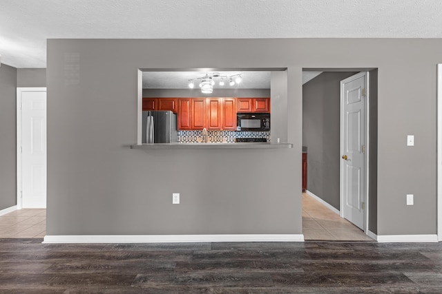 kitchen with black microwave, freestanding refrigerator, light wood finished floors, backsplash, and a textured ceiling