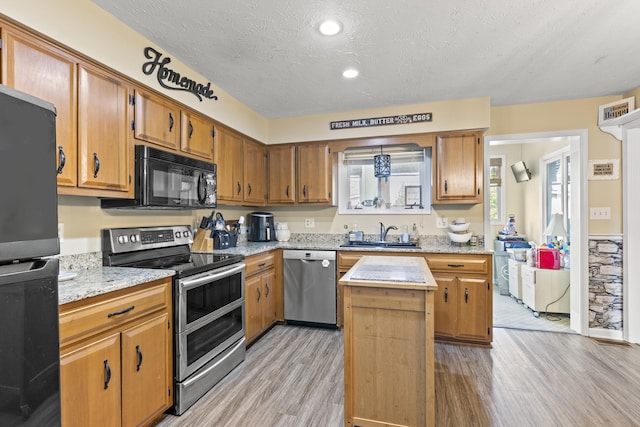 kitchen featuring black appliances, a sink, light wood-type flooring, a center island, and a textured ceiling