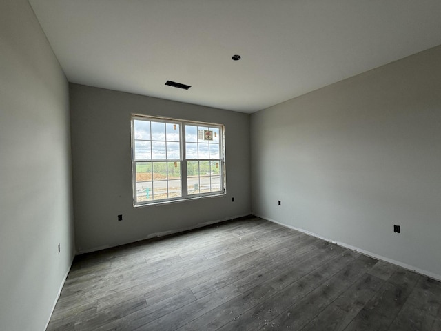 spare room with baseboards and dark wood-type flooring