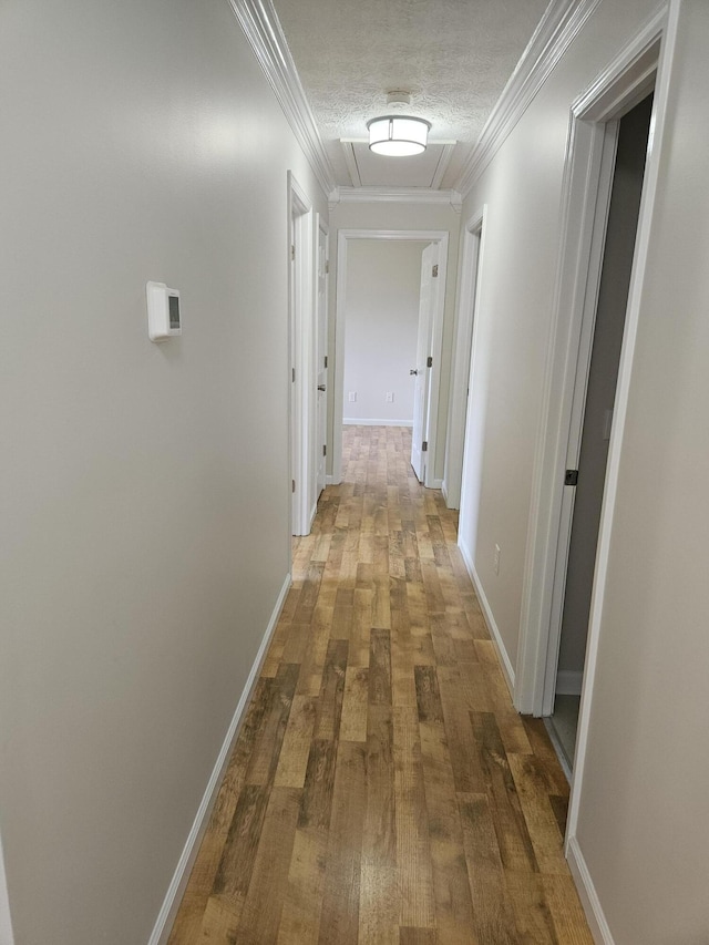 hall with wood-type flooring, a textured ceiling, crown molding, and baseboards