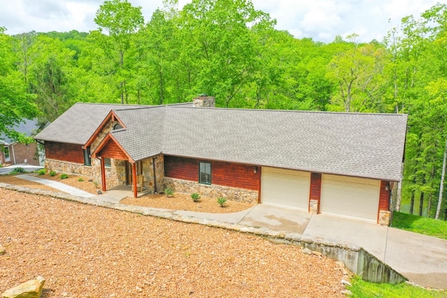 1117 Cliffs Edge Rd, East Bernstadt, KY 40729 - view of front facade with stone siding, a chimney, driveway, a shingled roof, and a forest view