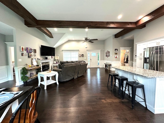 living area featuring dark wood-type flooring, wainscoting, ceiling fan, a fireplace, and a decorative wall