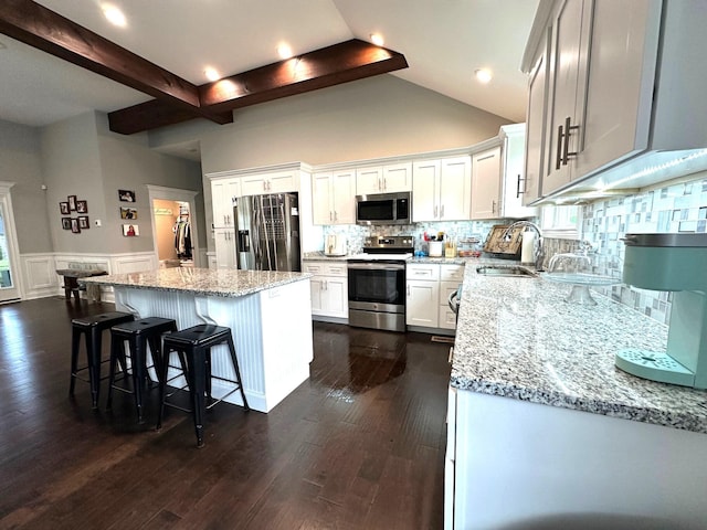 kitchen with appliances with stainless steel finishes, a sink, light stone countertops, a center island, and tasteful backsplash