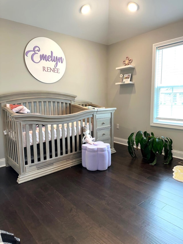 bedroom featuring dark wood-style floors, lofted ceiling, baseboards, and a nursery area