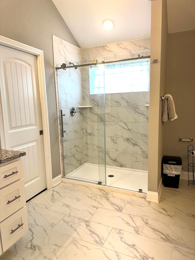 full bath featuring marble look tiles, a marble finish shower, baseboards, vaulted ceiling, and vanity