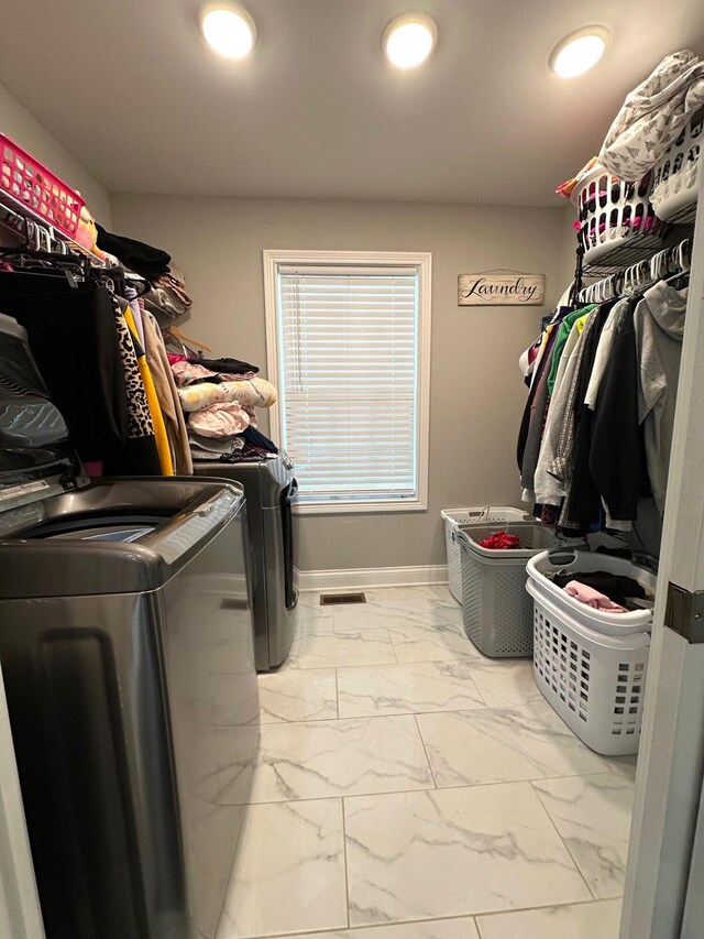 laundry room featuring washing machine and clothes dryer, marble look tiles, and baseboards