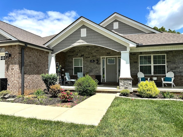 craftsman inspired home with a porch, a shingled roof, a front lawn, and stone siding