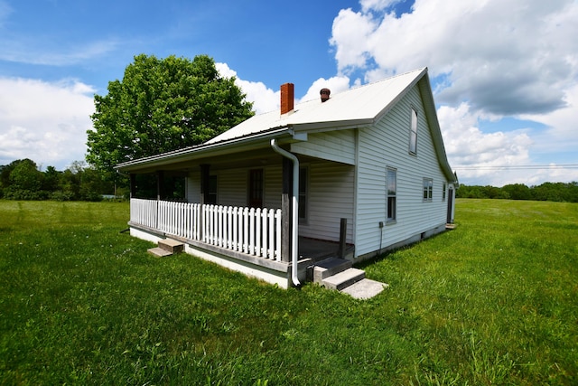 view of side of property featuring a porch, a lawn, metal roof, and a chimney