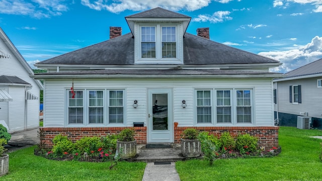view of front facade featuring a chimney, brick siding, a front yard, and a shingled roof