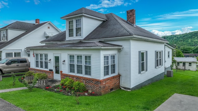 view of front of home featuring a front lawn, a chimney, brick siding, central air condition unit, and roof with shingles