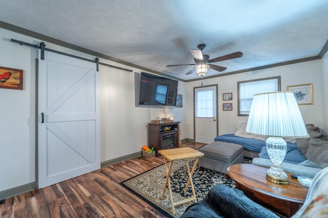 living room with ornamental molding, wood finished floors, a ceiling fan, a barn door, and baseboards