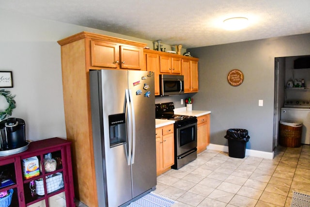kitchen featuring appliances with stainless steel finishes, light countertops, light tile patterned flooring, washer / clothes dryer, and baseboards