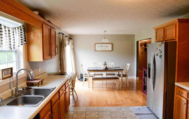 kitchen featuring stainless steel fridge, a sink, brown cabinets, a textured ceiling, and hanging light fixtures