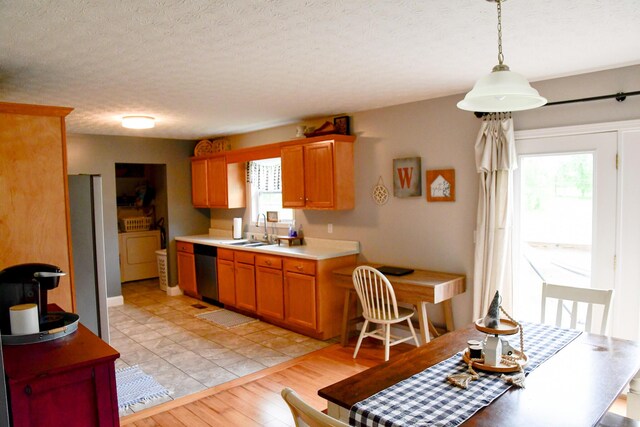 kitchen featuring appliances with stainless steel finishes, a sink, light countertops, light wood finished floors, and brown cabinetry