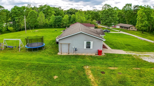 view of property exterior featuring a trampoline, a lawn, and a shingled roof