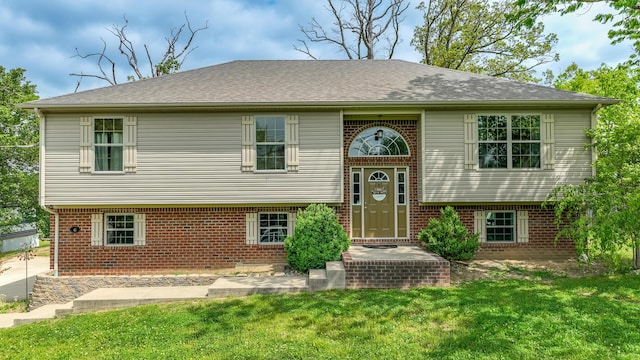 raised ranch with brick siding, a front yard, and roof with shingles
