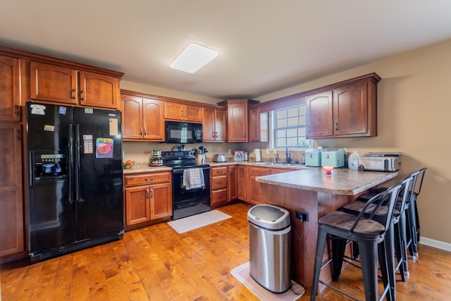 kitchen with black appliances, a peninsula, light wood-type flooring, a breakfast bar, and a sink