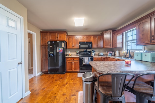 kitchen featuring black appliances, a sink, a peninsula, a breakfast bar, and light wood-style flooring