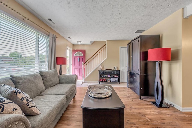 living area with light wood finished floors, stairs, baseboards, and a textured ceiling