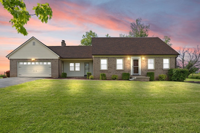 view of front of home featuring brick siding, asphalt driveway, a front yard, an attached garage, and a chimney