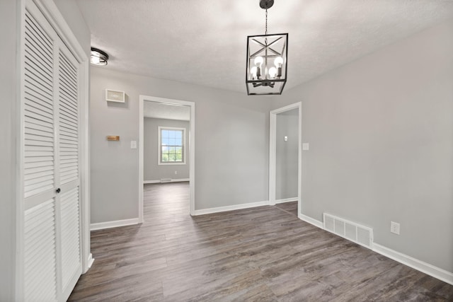 unfurnished dining area featuring a textured ceiling, baseboards, a chandelier, and dark wood finished floors