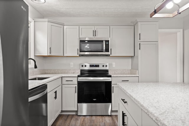 kitchen featuring appliances with stainless steel finishes, a sink, dark wood-style flooring, a textured ceiling, and light stone countertops