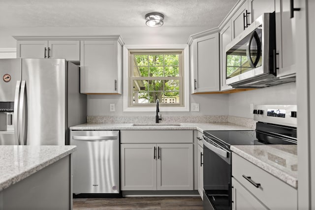 kitchen featuring appliances with stainless steel finishes, a sink, dark wood-style floors, a textured ceiling, and light stone countertops