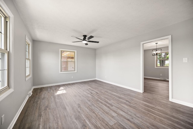empty room featuring dark wood-style floors, a textured ceiling, a chandelier, ceiling fan, and baseboards