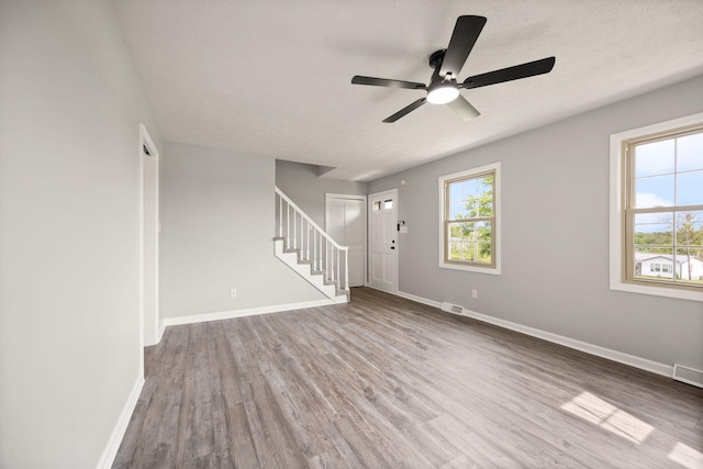 unfurnished living room featuring stairs, ceiling fan, plenty of natural light, wood finished floors, and a textured ceiling