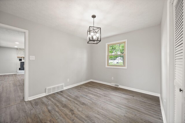 unfurnished room featuring wood finished floors, baseboards, a chandelier, a textured ceiling, and a brick fireplace
