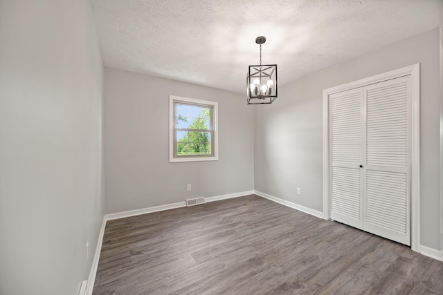 unfurnished dining area with a chandelier, dark wood-type flooring, baseboards, and a textured ceiling