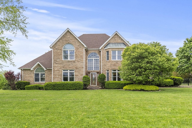 view of front facade with brick siding, a front yard, and a shingled roof
