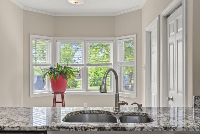 kitchen with a sink, stone counters, and ornamental molding