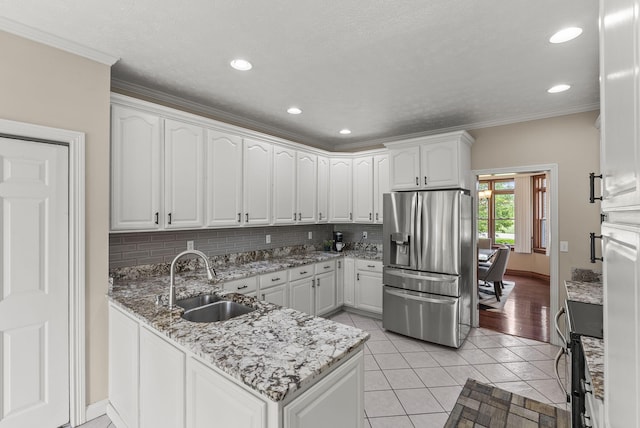 kitchen with stainless steel refrigerator with ice dispenser, a sink, a peninsula, decorative backsplash, and white cabinets