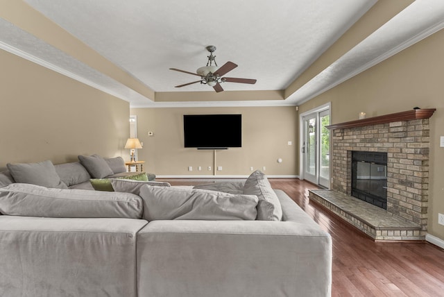 living room with a tray ceiling, ceiling fan, wood finished floors, and baseboards