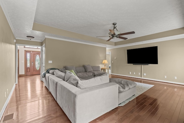 living area with a raised ceiling, a textured ceiling, a ceiling fan, hardwood / wood-style flooring, and baseboards