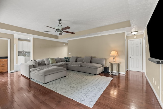 living area with a ceiling fan, dark wood finished floors, ornamental molding, a textured ceiling, and baseboards