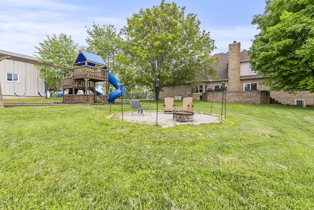 view of green lawn featuring a playground and a fire pit