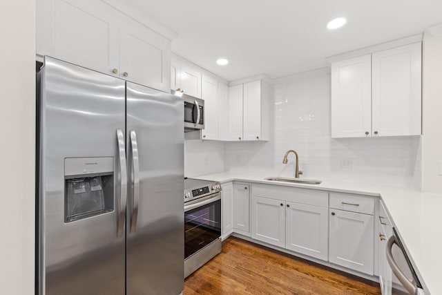 kitchen with stainless steel appliances, a sink, white cabinets, light countertops, and wood finished floors
