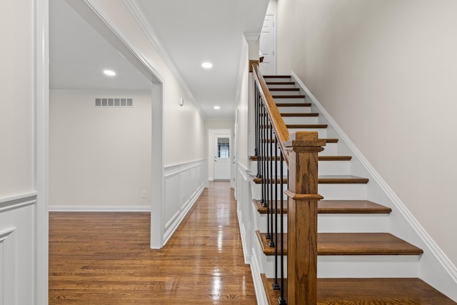 stairs with wood finished floors, ornamental molding, recessed lighting, and wainscoting