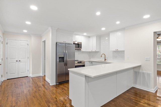kitchen with appliances with stainless steel finishes, a sink, a peninsula, white cabinetry, and ornamental molding