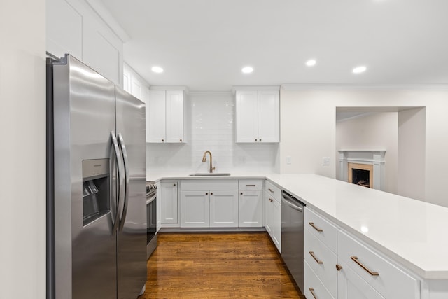 kitchen with appliances with stainless steel finishes, a sink, a peninsula, dark wood-style floors, and backsplash