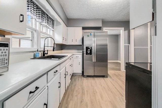 kitchen with stainless steel fridge, a sink, light wood-type flooring, light countertops, and a textured ceiling